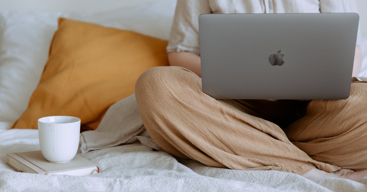 Online resource for duty-free - Crop faceless female in casual outfit sitting on bed with legs crossed holding laptop on knees with cup of coffee standing on notebook while working from home