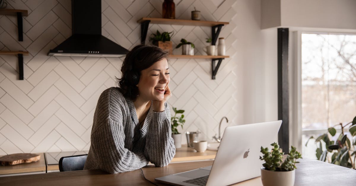 Online resource for duty-free - Young cheerful female smiling and talking via laptop while sitting at wooden table in cozy kitchen