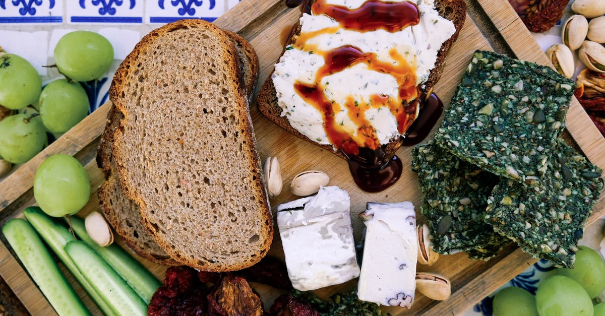 Organic Grocer in Tuscany? - Top view of wooden cutting board with fresh cucumber slices and black bread loafs with soft tofu cheese near dry seaweed and crunchy pistachios near pineapple guava