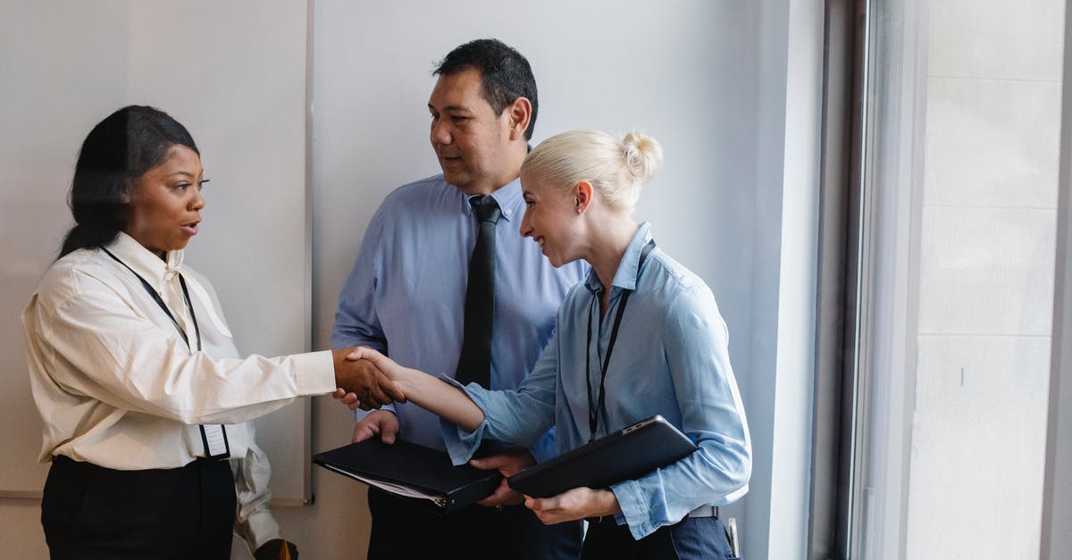 Original documents for UK visa biometric appointment - Happy young multiethnic female managers in classy outfits smiling and shaking hands during meeting with ethnic colleague in office