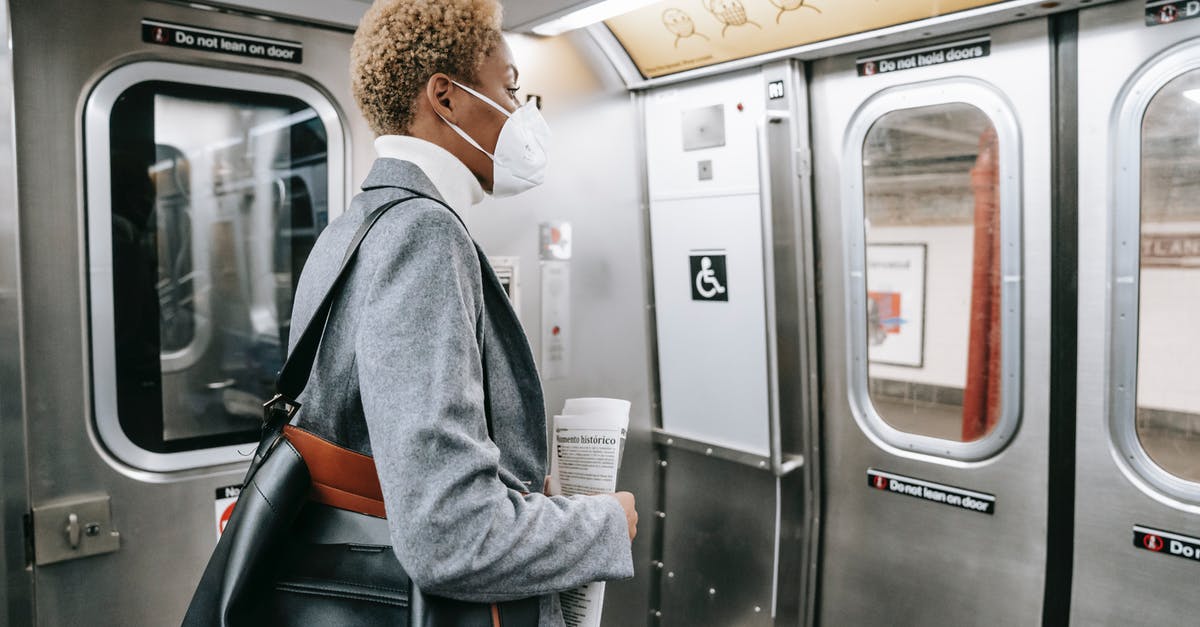 Overnight train luggage safety concerns in Europe - Back view contemplative young African American female in stylish wear and face mask standing with handbag and newspaper and riding subway train