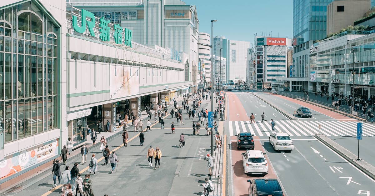 Owning a car in Japan and changing visa/departing for a long trip - From above of unrecognizable people walking near road and modern Shinjuku Station located against cloudless blue sky in Tokyo