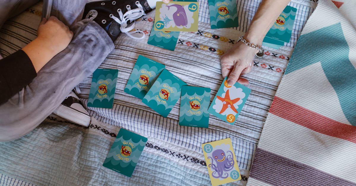 Oyster card vs Travelcard from Woking for a weekend - Top view of crop anonymous kid with mother playing card game with colorful marine pictures on bed during weekend at home