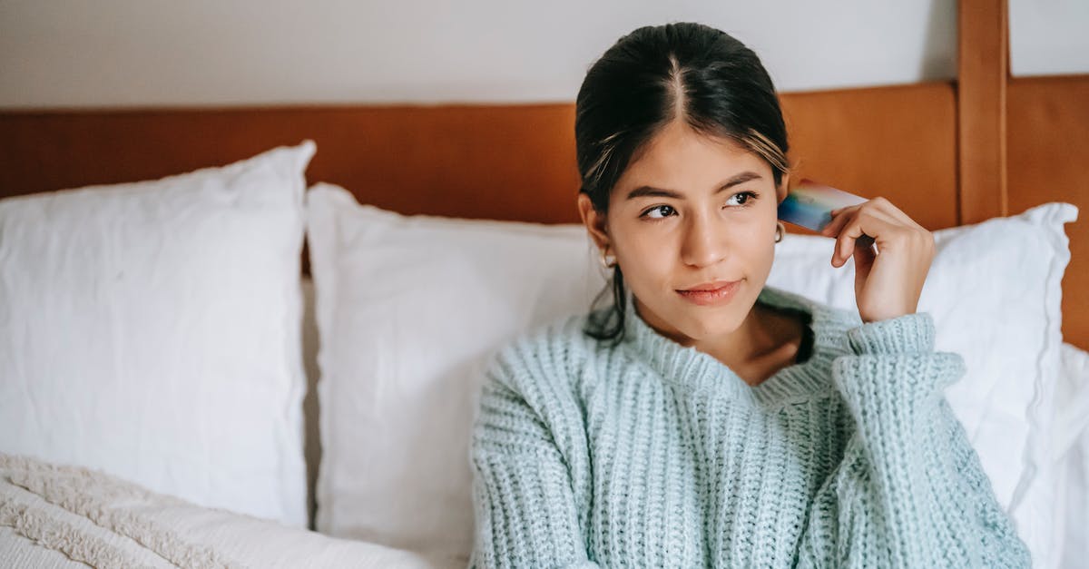 Oyster card vs Travelcard from Woking for a weekend - Young contemplative ethnic female with plastic card sitting on soft bed while looking away in house