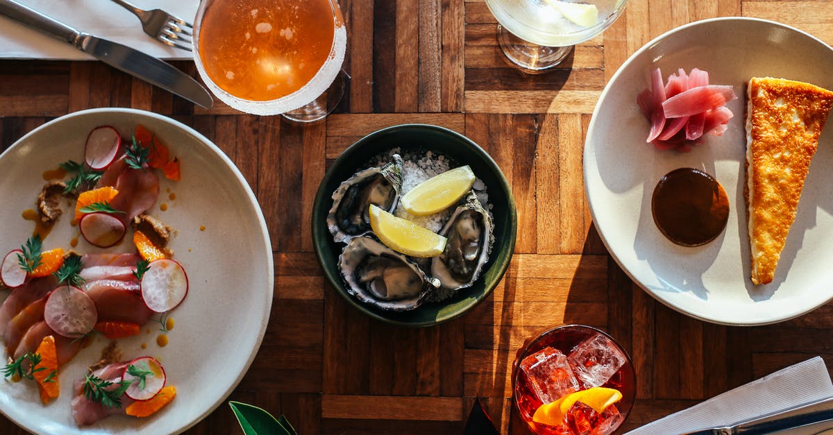 Oyster or travelcard for 5 days? - Top view of assorted cocktails and bowl of oysters served on wooden table near plate of fresh raw sliced fish and yummy dessert