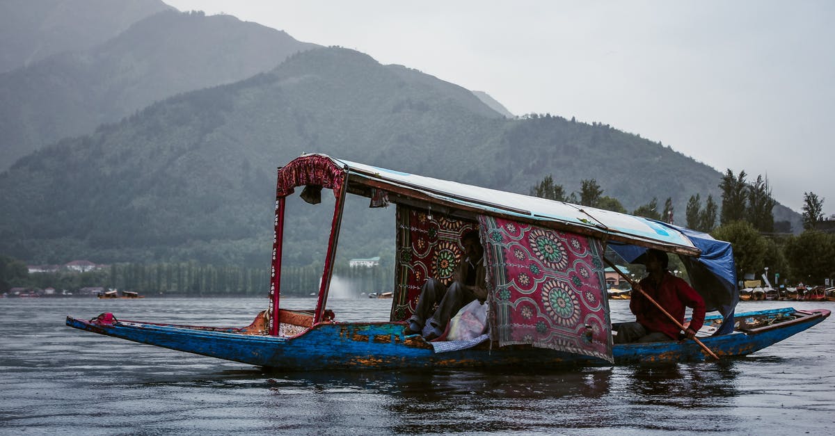 Pakistani travelling to Indian Kashmir? - Anonymous ethnic men in roofed boat on lake against ridge