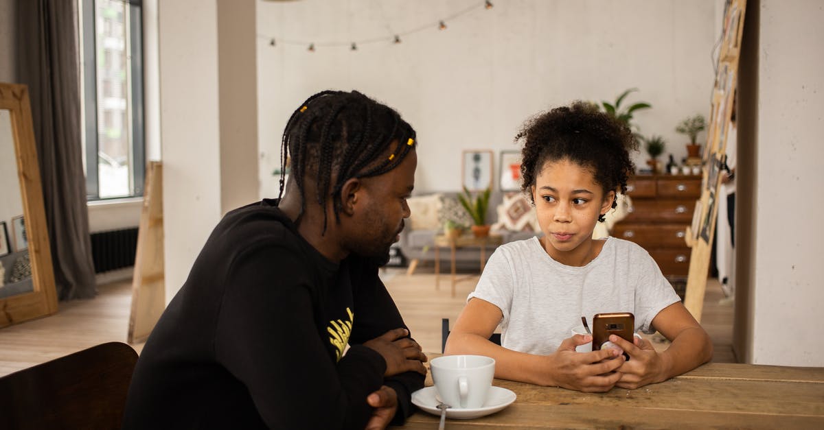 Parent-child; sit next to each other on an all-inclusive flight? - African American man sitting at table with cup of coffee and talking to daughter browsing cellphone