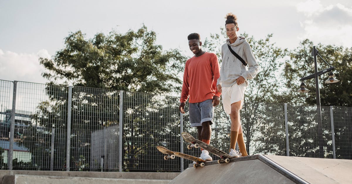 Park & Ride in Düsseldorf, coming from Belgium/Netherlands - From below of happy multiethnic friends standing on tail of boards before performing extreme stunt on ramp in skate park on summer day