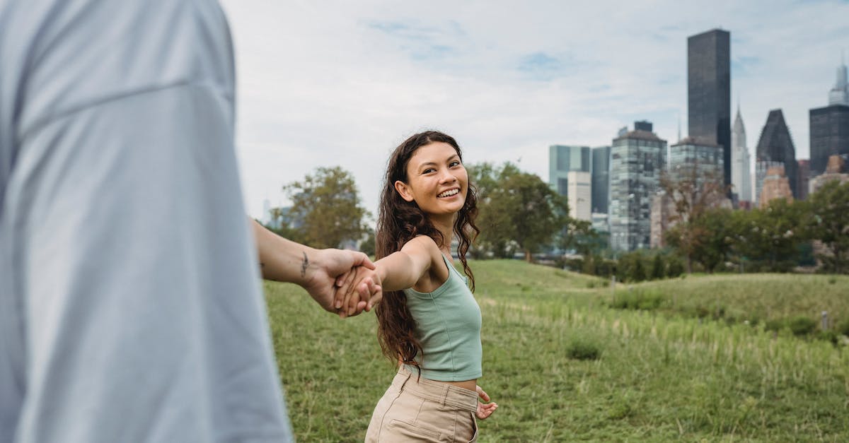 Park City, Utah for vacation - Crop anonymous man holding hand and following happy young ethnic girlfriend while spending time together in green park in New York