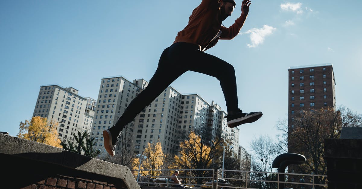 Parkour - Tricking - Free-running in Tokyo? - Side view energetic young male tracer in casual clothes jumping from brick fence against modern city buildings on clear sunny day