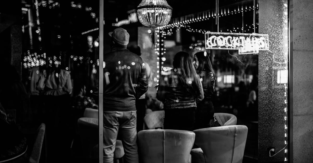 Party going through airport security at separate times? - Black and white of young anonymous people spending time in bar with bright lights at night