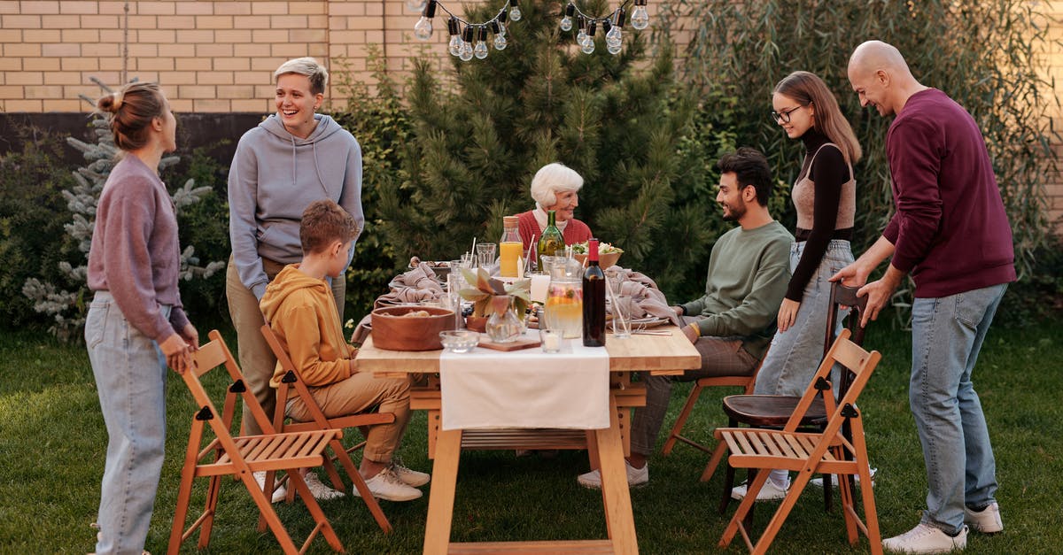 Party going through airport security at separate times? - Happy family members talking and sitting down to eat tasty food at big wooden table in backyard in daytime