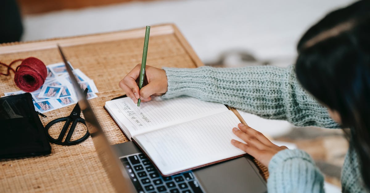 Passport stamp - France Study Visa and Stopover in Spain - High angle of anonymous ethnic female student in casual outfit taking notes with pen in notebook near laptop at table near scissors and ball of yarn on stamps at home