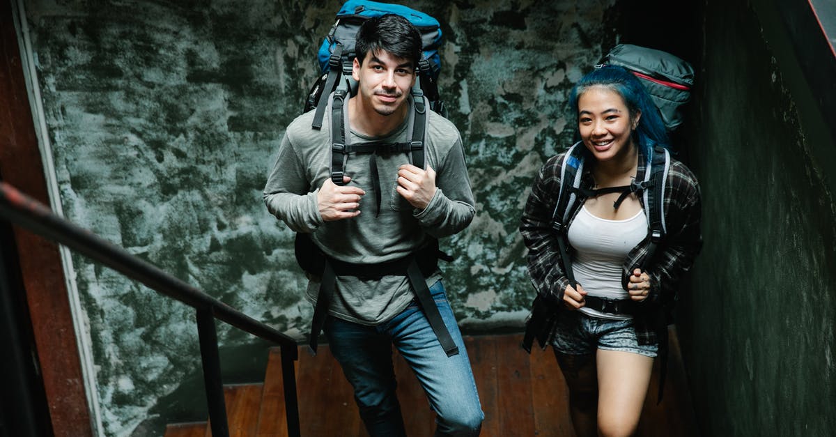 Photo backpack as first carry-on luggage for travelling with Ryanair [closed] - From above of positive diverse couple of travellers with backpacks standing together on narrow wooden staircase