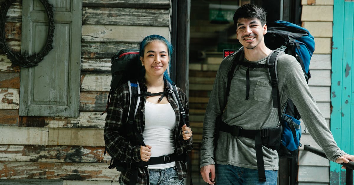 Photo backpack as first carry-on luggage for travelling with Ryanair [closed] - Young smiling diverse couple of travelers in casual clothes and with backpacks standing together near wooden wall in light room and looking at camera