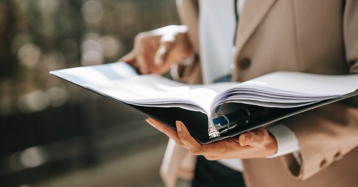 Photocopies of important documents stolen - Crop faceless female entrepreneur in formal jacket turning pages of documents in folder while reading