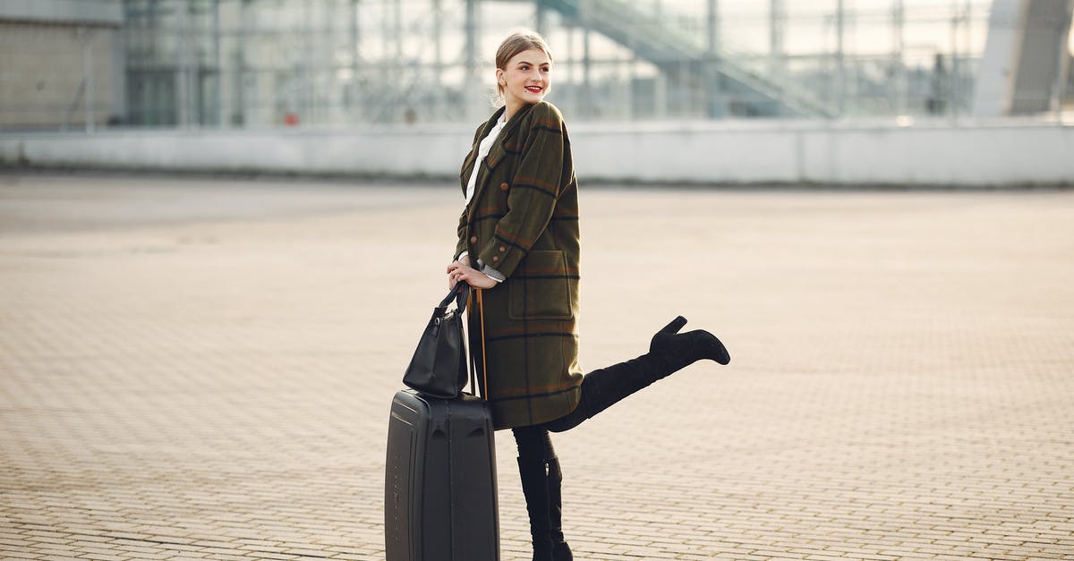 Pick Up Wheelchair Passenger at SFO airport - Full body of stylish female tourist in warm clothes and high heeled boots standing on background of blurred airport terminal with luggage and ladies bag