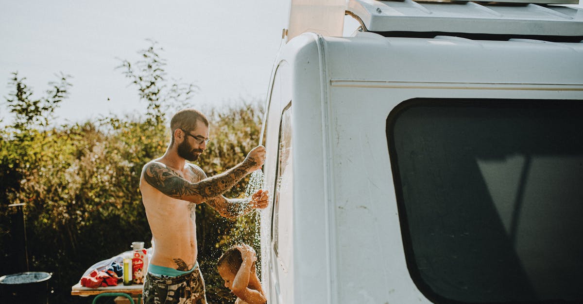 Places for camping without a caravan in UK -  Man with Tattoos Giving Shower to His Son in front of the Caravan