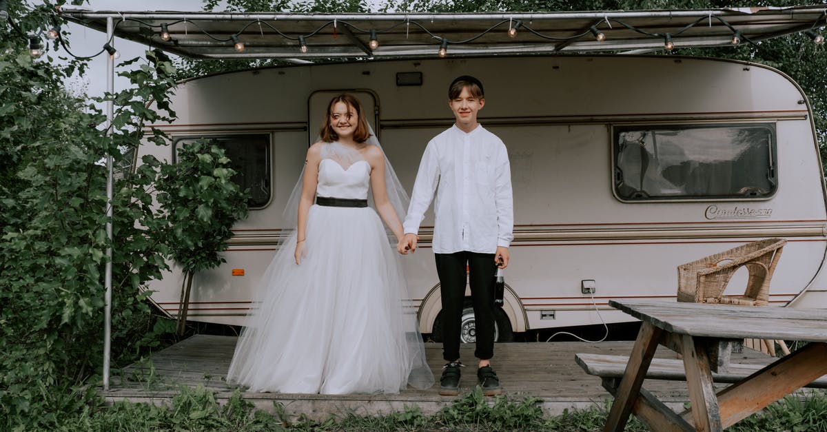 Places for camping without a caravan in UK - Woman in White Wedding Dress and Man in White Shirt Holding Hands While Sanding Beside Caravan