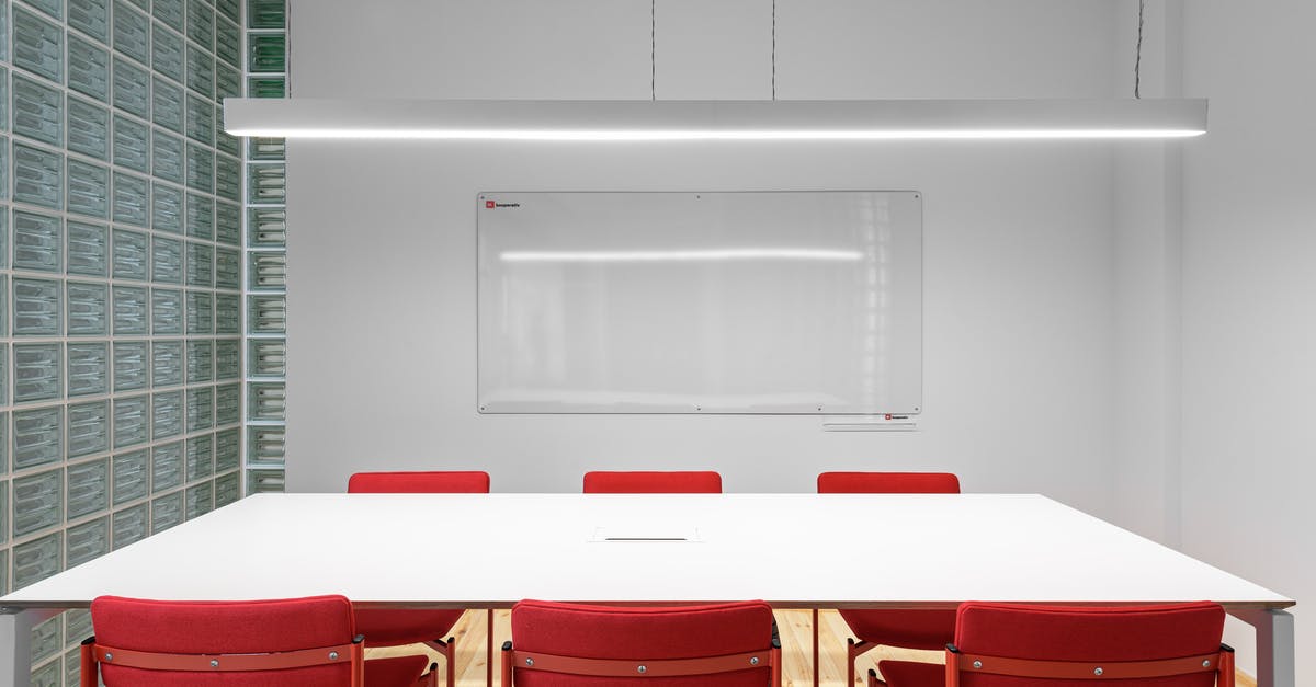 Places to seat/sleep at SFO pre-security - Interior of office with white table near red stools and whiteboard on wall near lamp and glass wall