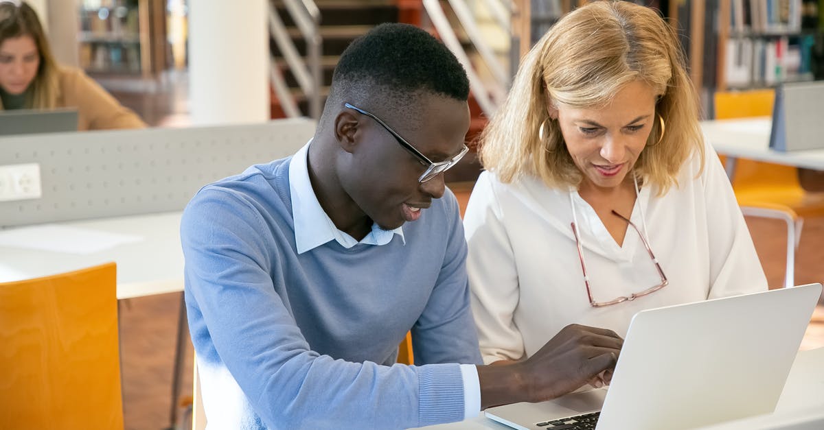 Please explain the local library system in London, England - Female teacher helping ethnic male student working on laptop in library