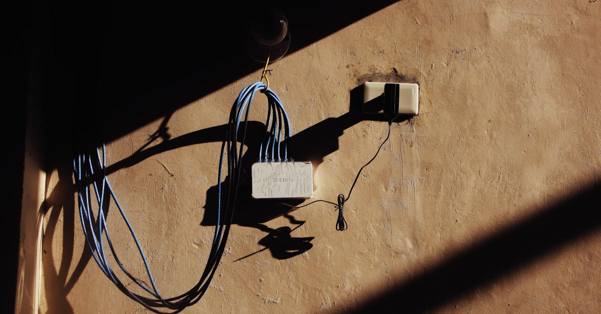 Plugging in a Power Spike/Surge protector to a Voltage Converter - Electric blue wires connected to network adapter plugged in socket on shabby brown wall of building on street with shadow