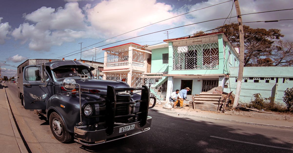 Post forwarding in the UK - Aged pickup vehicle on rough roadway against building facade and unrecognizable ethnic partners under blue cloudy sky in town