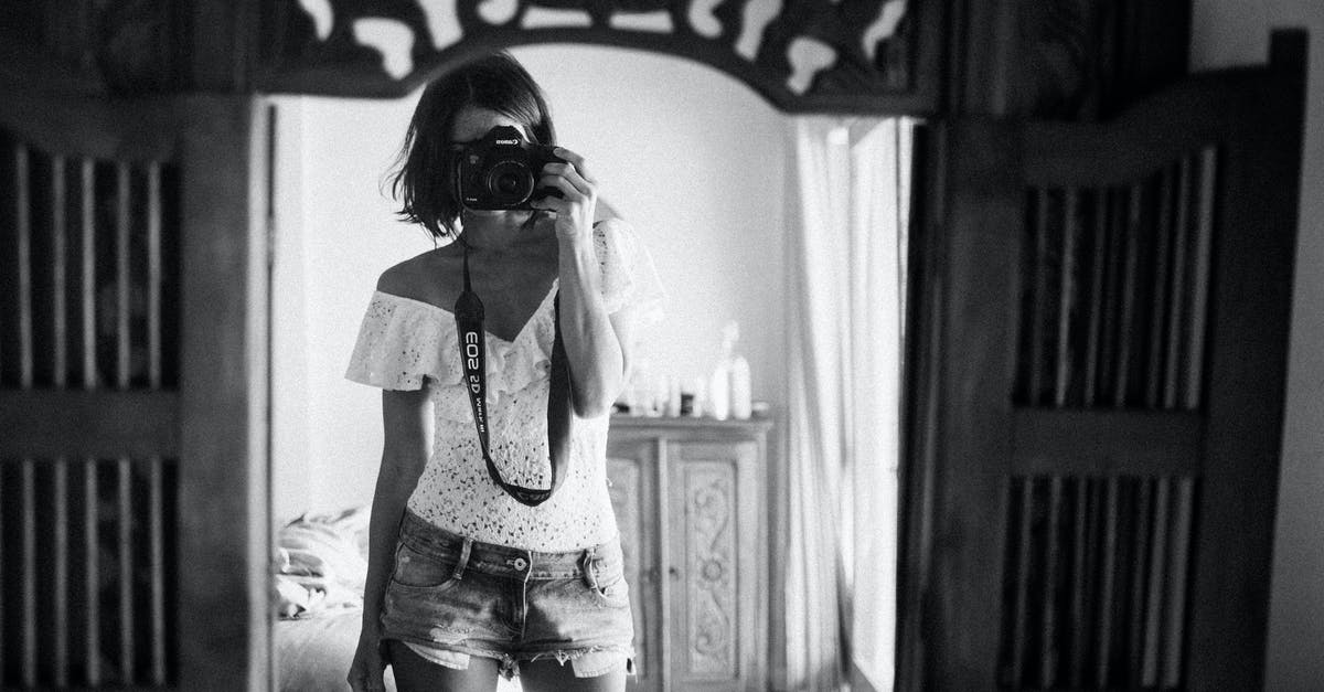 Precautions to take when travelling alone around Ireland - Black and white of casual female photographer in summer clothes standing against mirror in light room and taking photo with camera