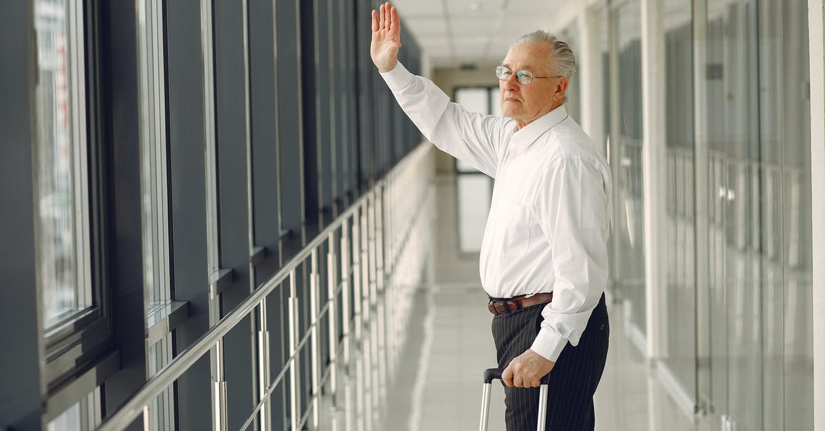 Premier inn old Trafford to Manchester airport [closed] - Side view of aged calm male in formal clothes with suitcase walking along modern airport hallway and waving goodbye while looking out glass wall