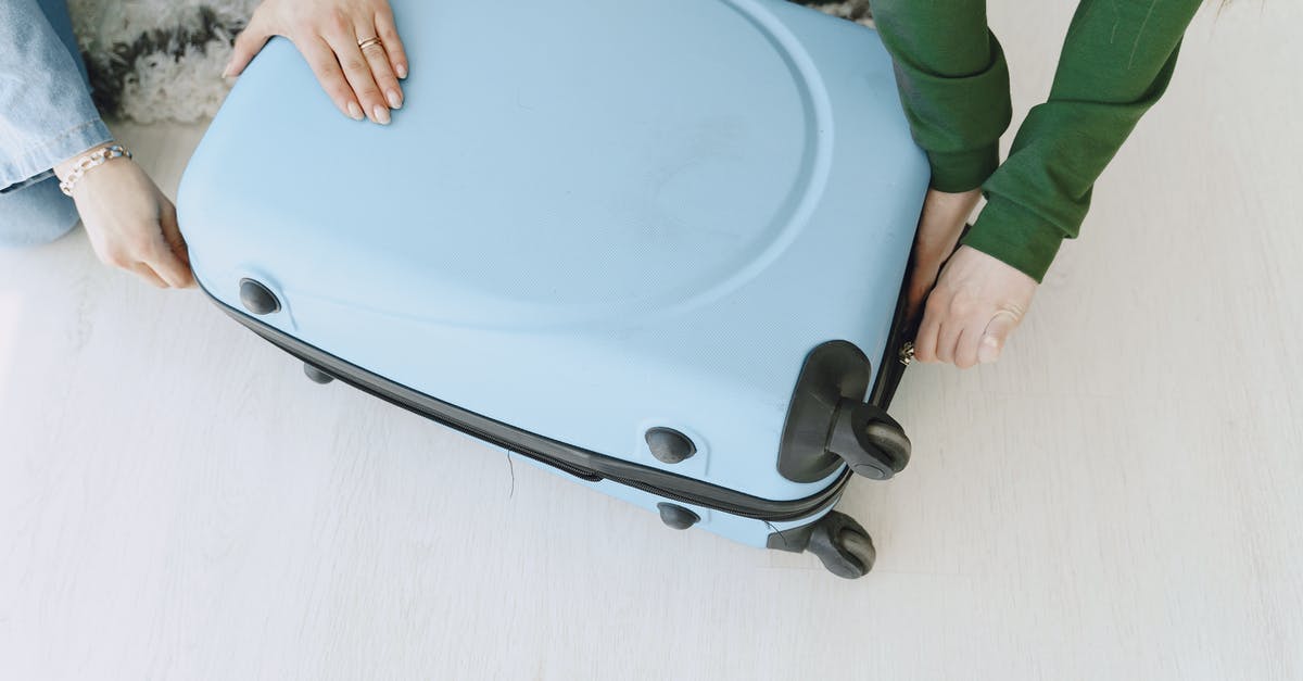 Preparing home for your trip - Unrecognizable female friends in casual clothes sitting on floor with fluffy carpet and opening suitcase together while preparing for journey and adventure