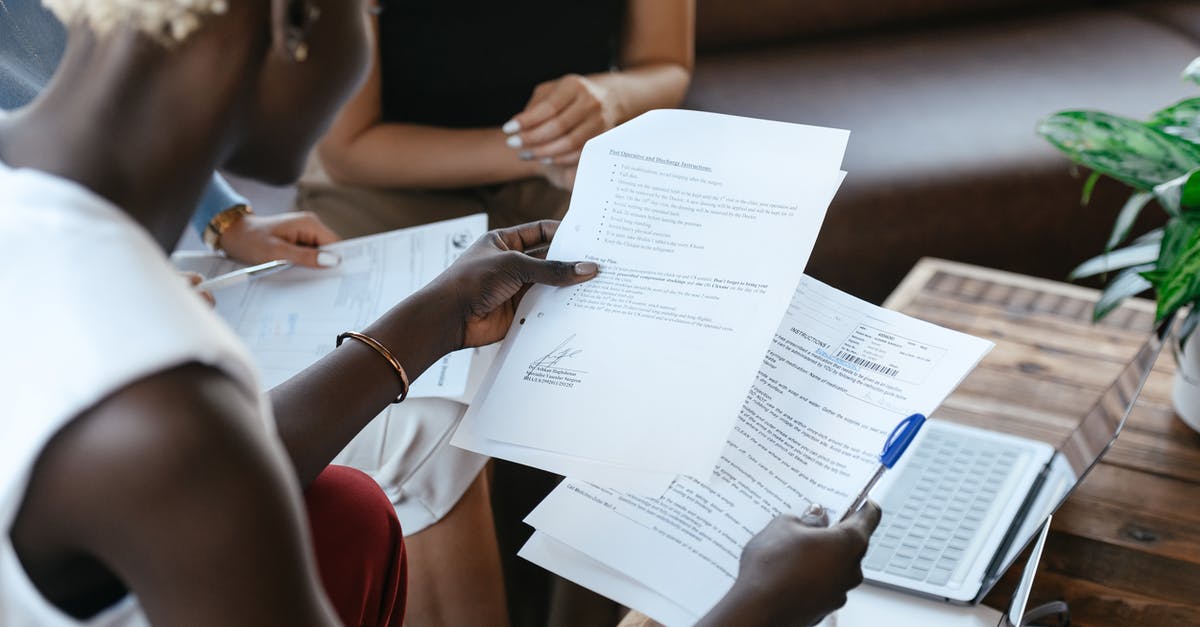 Previous employment data in DS-160: listing a defunct company - From above of crop anonymous African American female comparing data in papers at table of office