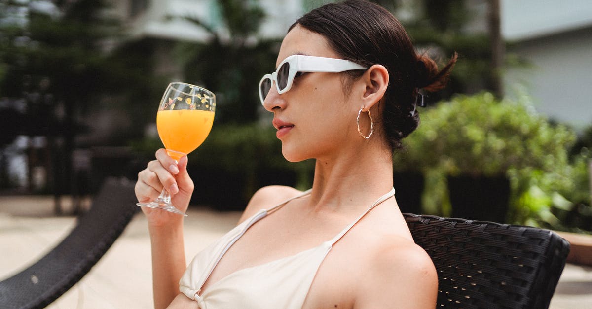 Price limits for self-arranged hotel after flight cancellation - Stylish young ethnic woman drinking smoothie while chilling on sunbed in resort