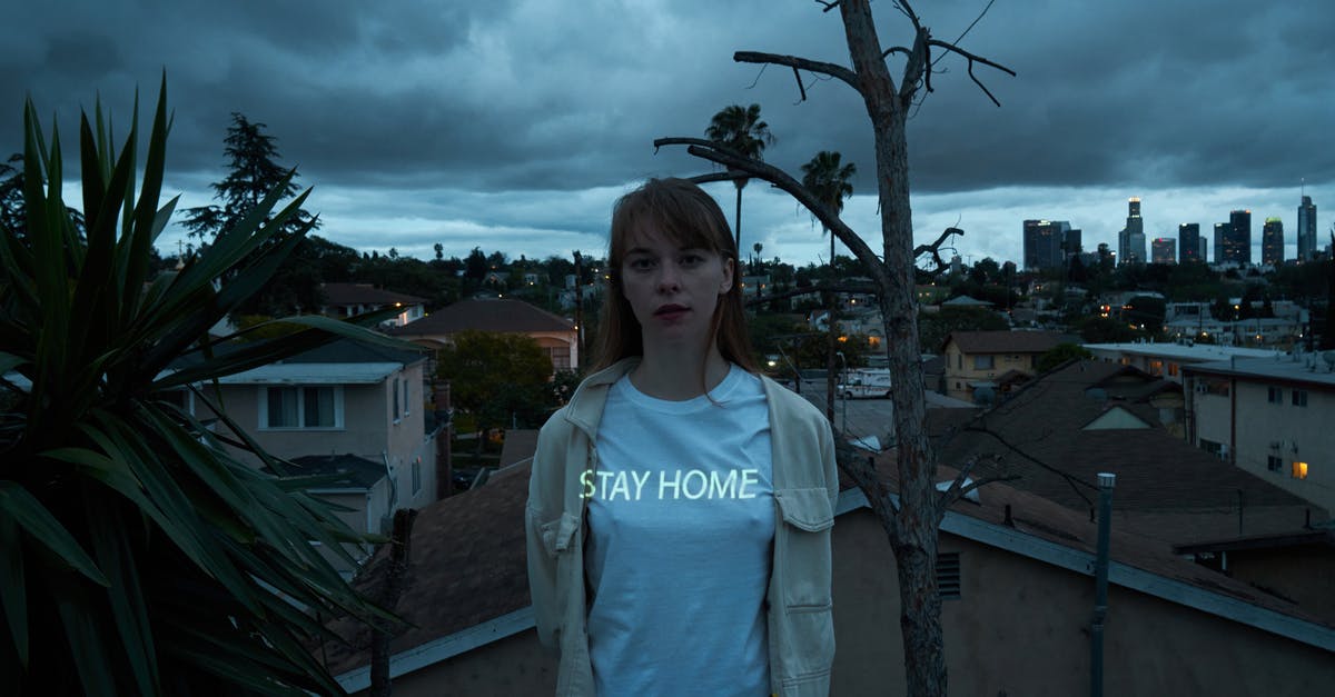 Problem at filling self declaration COVID – 19 Italy - Young calm female in casual white shirt with illuminated stay home text standing on roof against night cityscape and looking at camera thoughtfully coronavirus concept