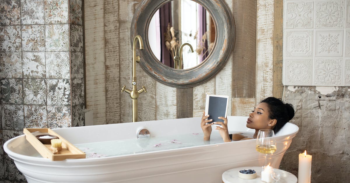 Procedure and time frame to get a credit card replaced - Young African American female reading book while taking bath in light bathroom with burning aromatic candles placed near round table with wineglass and berries on background of shabby stone walls