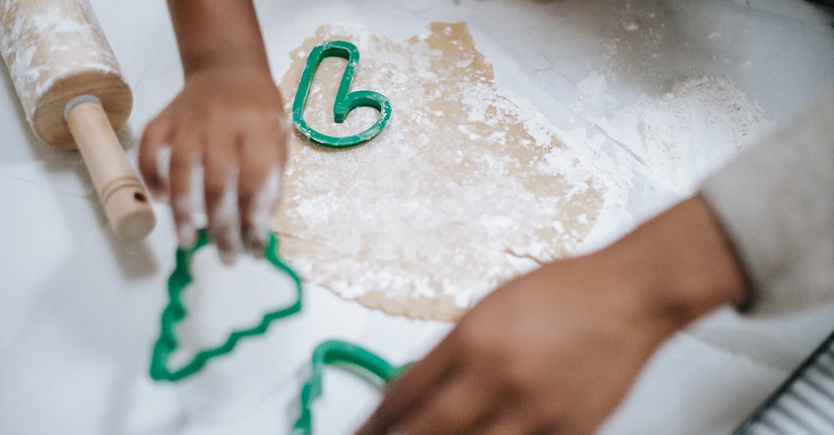 Processing time of a working holiday visa in New Zealand - From above of crop anonymous black kid and parent using decorative pastry cutters on table with dough