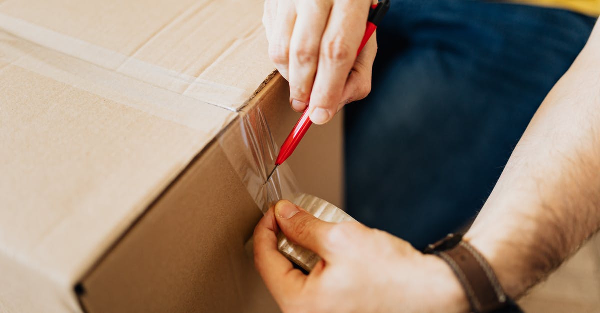 Prohibited Parcel Items from the UK to Ukraine [closed] - From above crop anonymous male sealing packed carton boxes by using tape and cutter knife while preparing for moving in new apartment