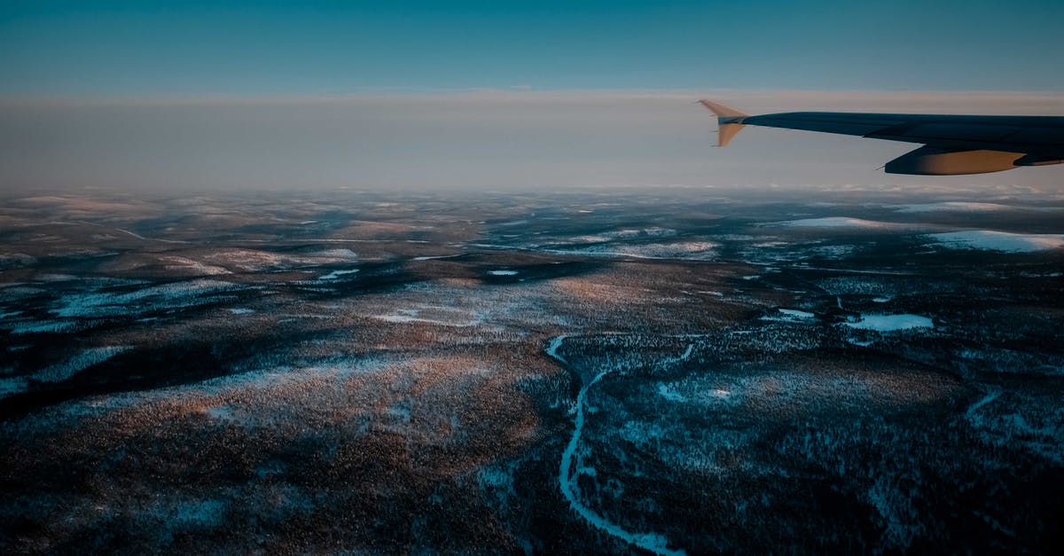 Proof of onward travel by flight from another country - View from airplane of wild snowy valley with curvy frozen rivers located in vast deserted terrain in winter evening