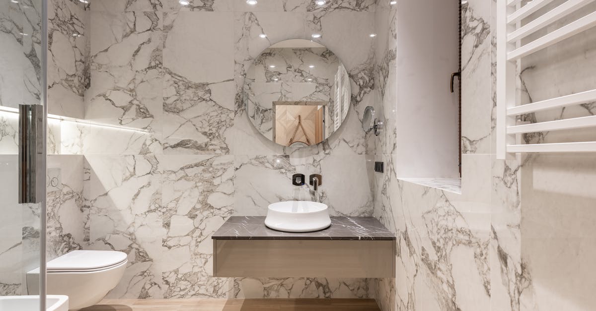 Proper technique to wash laundry in hotel sink? - Interior of modern bathroom with round mirror hanging on marble wall and white ceramic sink and toilet bowl