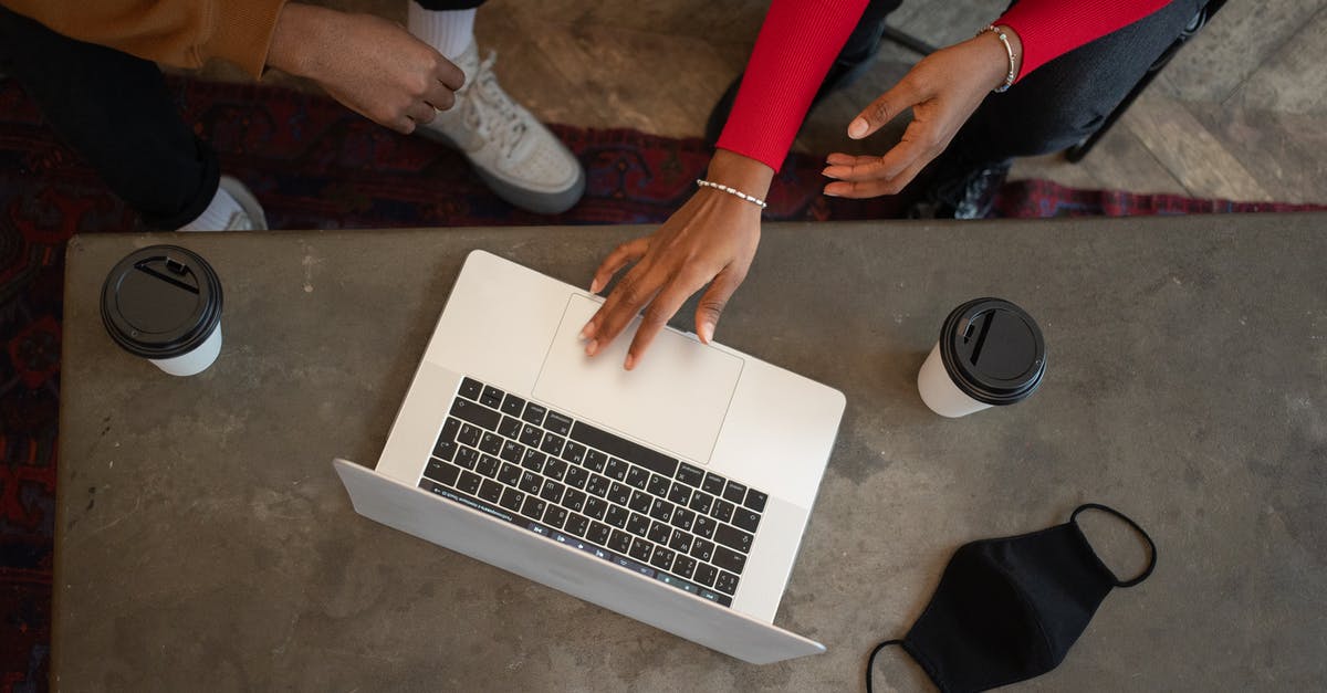 Protect laptop (and fellow passengers) from turbulence? - Top view of crop anonymous African American coworkers surfing netbook while sitting at table with medical mask and takeaway cups of coffee during work