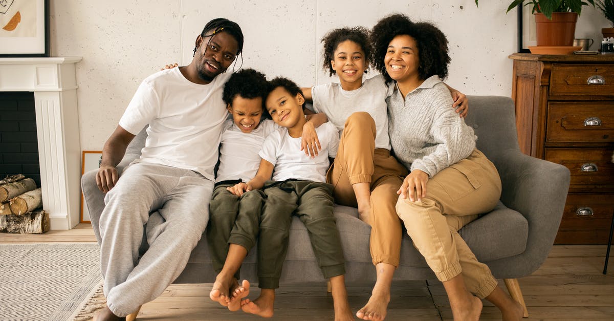 Proving sibling relationship - Full body of cheerful African American parents with children looking at camera while sitting on sofa in room with fireplace