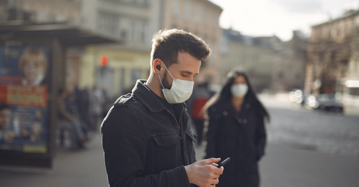Public transport connections to San Francisco after Caltrain stops running - Focused man in medical mask using smartphone on urban street in cold season