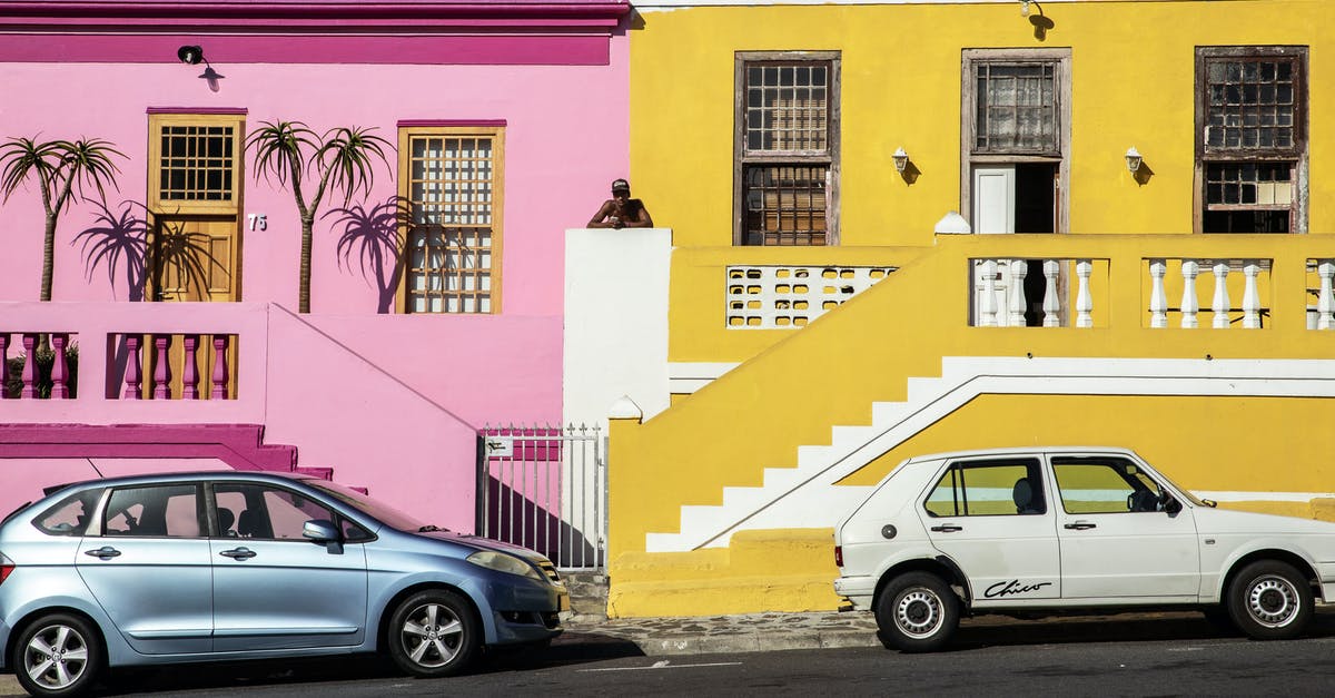 Public transport options between Paris and EuroDisney - Distant African American man standing between pink and yellow residential buildings located near road with parked cars on street in town