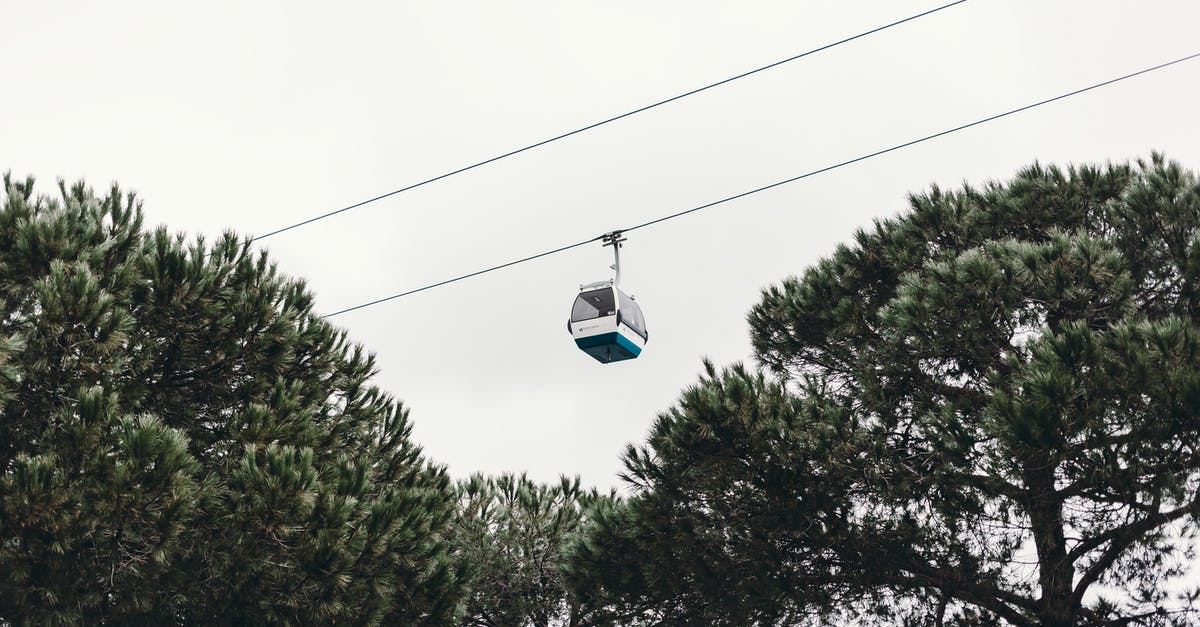 Public transportation from La Paz to Mt. Chacaltaya - From below of modern cable car over green trees under cloudy sky in daylight