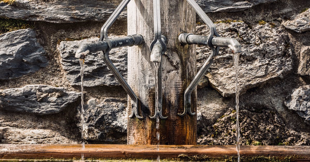 Public water taps in Palmer AK - Metal taps of fountain with pouring water into tank placed on wooden post near stone wall on street in city