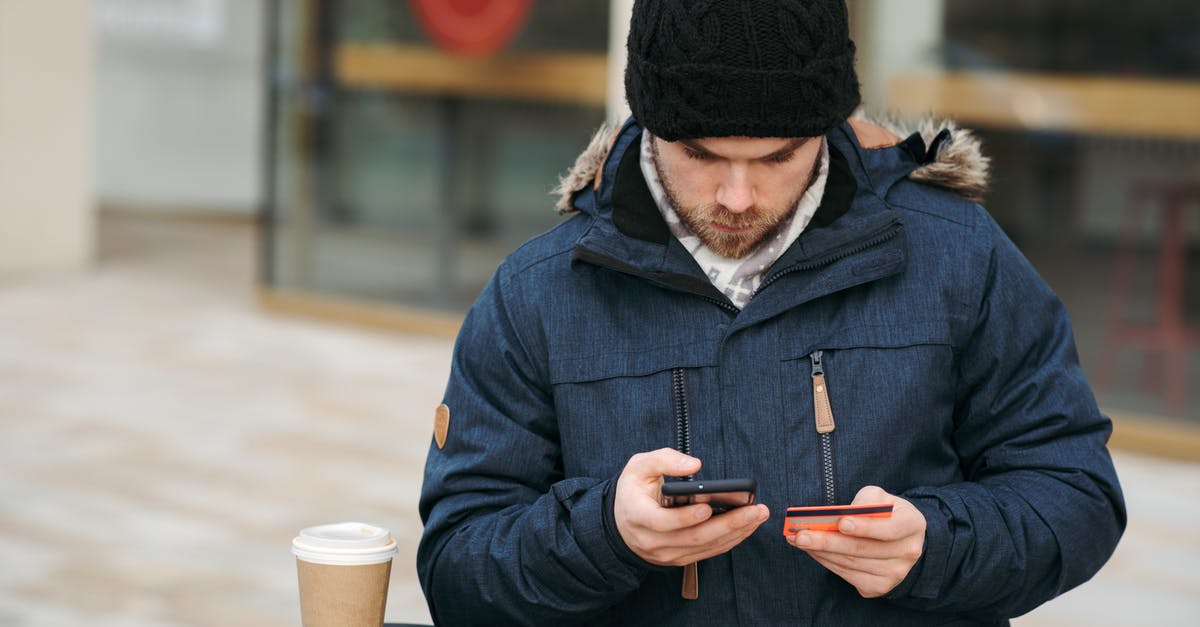 Purchase tickets, Prague to Brazil, but using Bank Transfer - Focused male holding credit card while making payment with smartphone on street