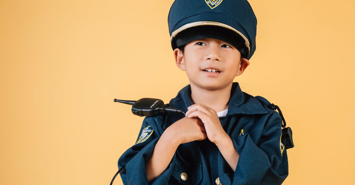 Purpose of the 'Witches' Hats' on the A13 in London - Pleasant Asian boy in police uniform and cap looking away while standing with hands near chest in studio on yellow background