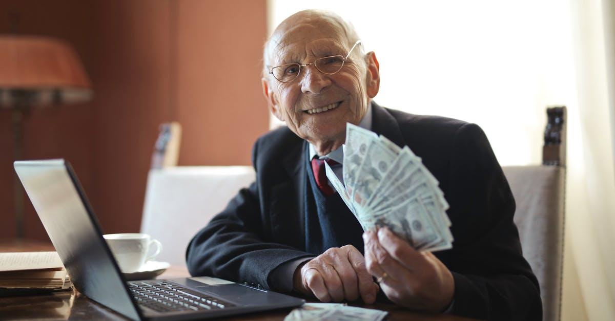 Putting a hold on an airline seat - Happy senior businessman holding money in hand while working on laptop at table