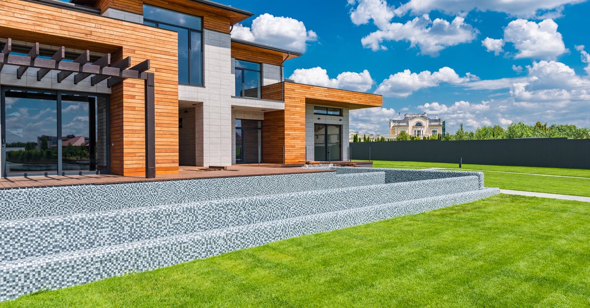 Queenstown, New Zealand private transfers - Exterior of contemporary residential house with panoramic windows glass doors and green lawn in yard on sunny day against blue sky with white clouds