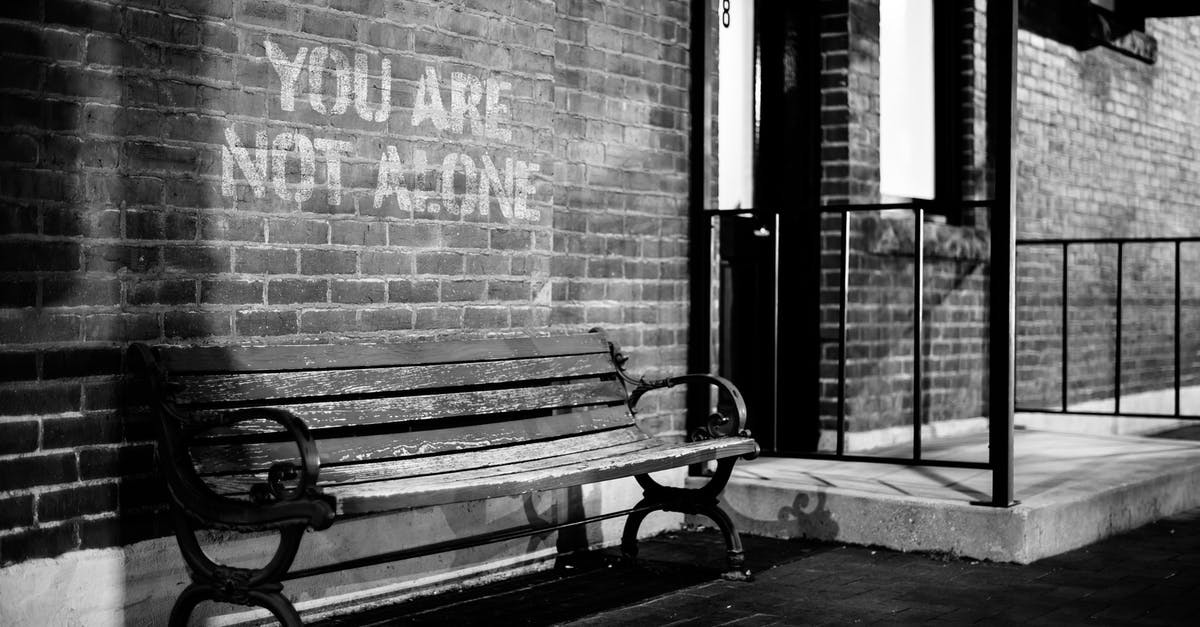 "Any Belgian Station" destination on the Eurostar - Black and white of empty wooden bench near brick wall of building with inscription you are not alone