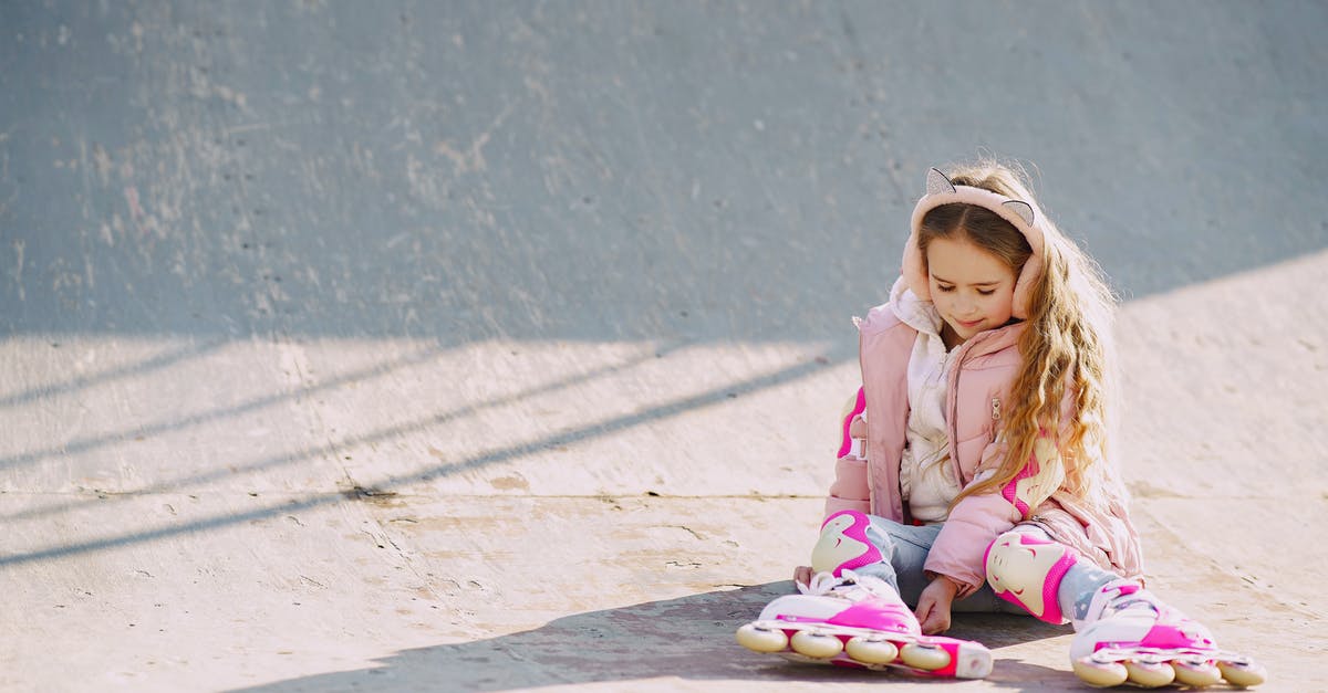 "Park and Ride" options to visit London? - Glad little girl wearing warm pink jacket and protective pads looking down on rollers while sitting on concrete surface of ramp for skating during visiting skate park in sunny cold day